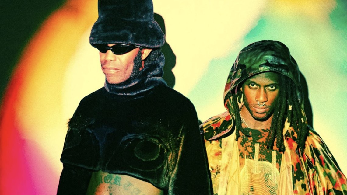 Experimental punk/hip-hop duo Ho99o9 stand against a bold, high contrast background set against psychedelic lighting.